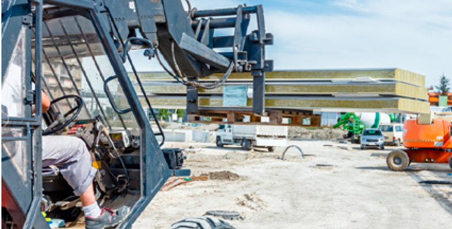 Worker operating a hoist to lift building materials at an active construction site, with scaffolding and partially built structures visible in the background.