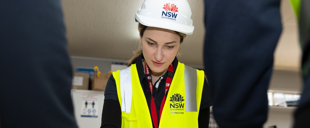 safework inspector wearing a white hard hat and yellow vest viewing plans