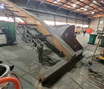 A bridge crane inside a warehouse, collapsed on its side.