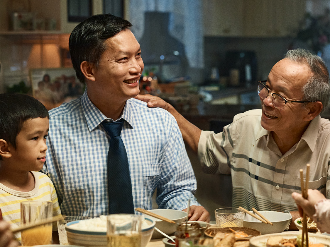 Man in blue shirt and tie smiling around the dinner table with his relatives