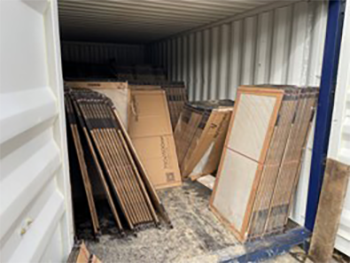 Inside a shipping container, multiple tiles are stacked vertically and leaning in various directions, creating an uneven and potentially unstable arrangement.