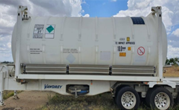 A white cryogenic tank container mounted on a trailer in an open field, displaying multiple danger warning stickers.