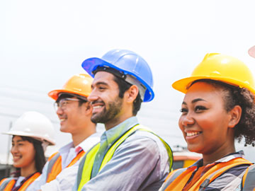 A multicultural group of workers wearing construction PPE, smiling. 