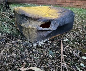A black petrol can lies on the ground with a blown hole at the bottom, indicating damage from an explosion or pressure buildup.