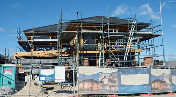 House construction site surrounded by scaffolding and ladders. The site is fenced off for safety.