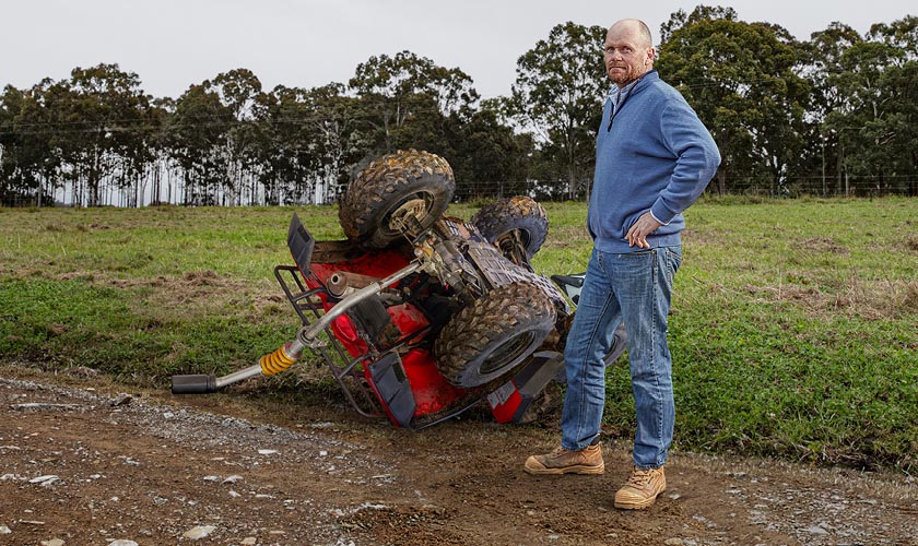 Man standing next to upturned quadbike on rural property