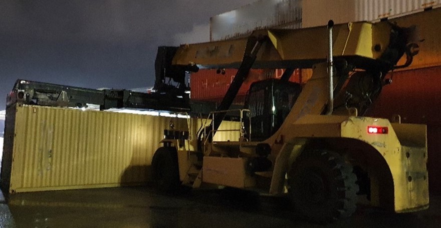 A yellow reach stacker near a shipping container