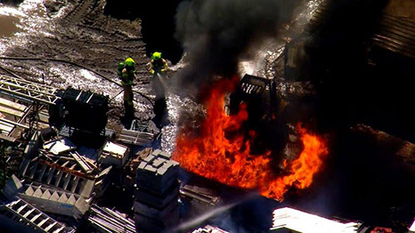 Aerial image of a manufacturing facility with flames and smoke above.