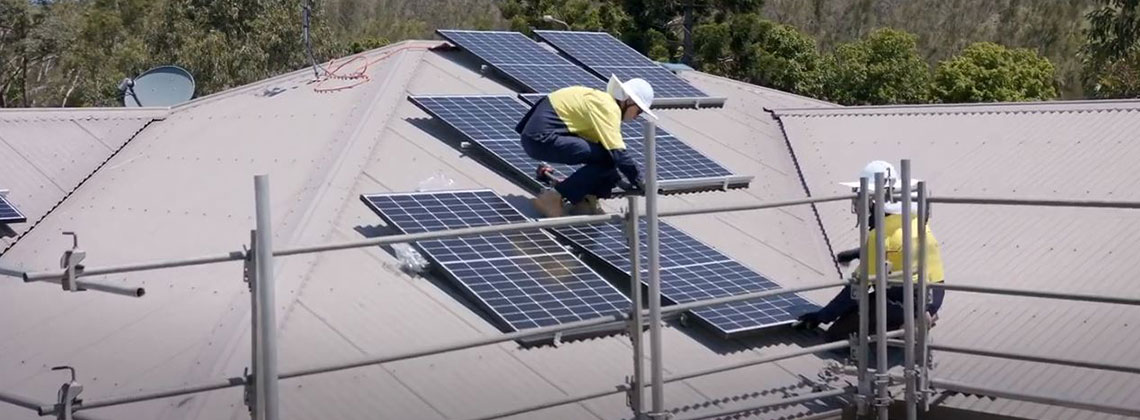 Two workers installing solar panels on a roof, surrounded by fall protection guard rails. 