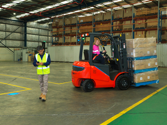 A worker wearing high vis walking away from a loaded forklift that is being driven by a worker in high vis.