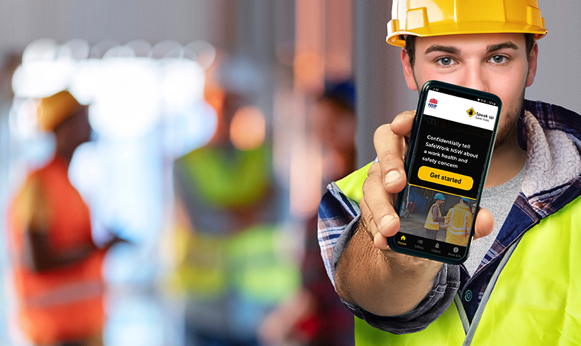 A campaign image of a young worker holding a mobile phone with the Speak Up Save Lives app