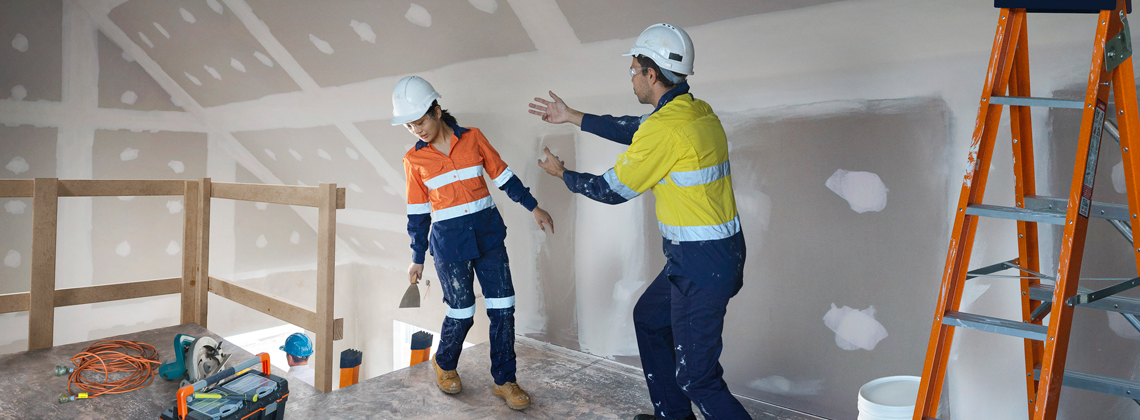 Two workers wearing hard hats and high vis, pictured near a void. One worker appears to be stumbling backwards, with the other worker attempting to reach them.