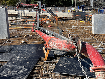 East-face view of a concrete truck incident at a construction site, showing the boom and red pipe attached to it lying on the ground, with multiple wireframes in the background.