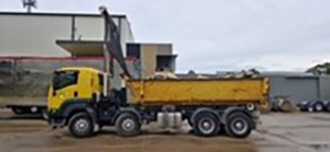 A side view of a yellow skip-bin truck at what appears to be at a truck depot, the location where the accident occurred.
