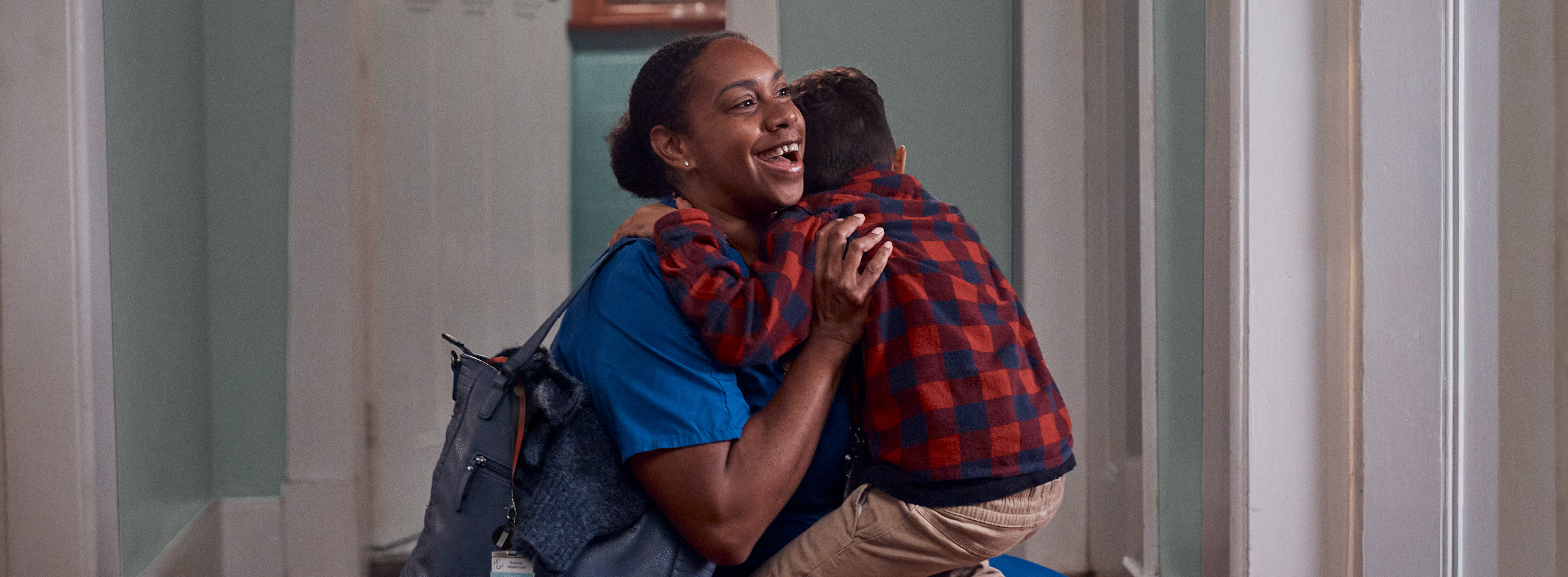 Medical worker wearing blue scrubs kneeling down to happily greet her young son