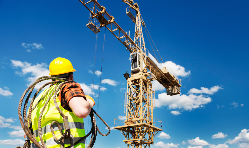 A crane dogman carrying a wire rope to a large tower crane