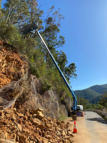 An elevating work platform (EWP) positioned on an unsealed embankment, extended towards high trees