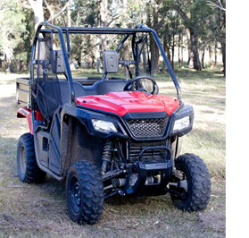 A red and black farm vehicle photographed from the front, position on a dirt road with trees in the background.