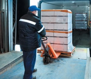 Photo of a worker using a pallet jack and tailgate lifter to load stock into a truck