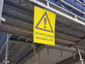 A yellow warning sign on a building under construction saying 'Scaffolding incomplete'