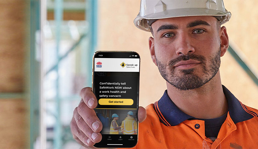 A worker on a construction site, holding a phone up with the Speak Up Save Lives app open