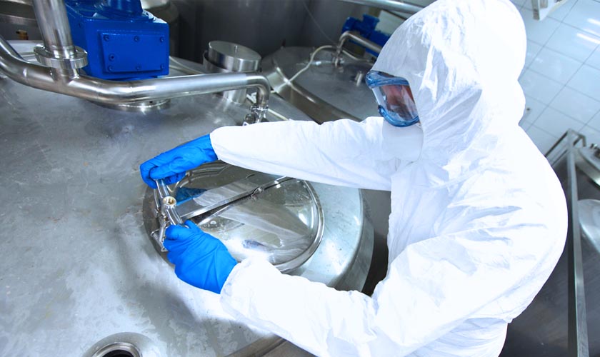 A person in a protective suit with goggles and gloves closing the lid on a large stainless steel vault