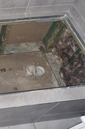 Top-down view of a bathroom with brown tiles, showing an unfinished bathtun holder with exposed wooden framework