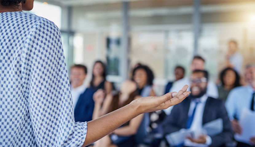 A worker standing in front of a room, giving an informal presentation.