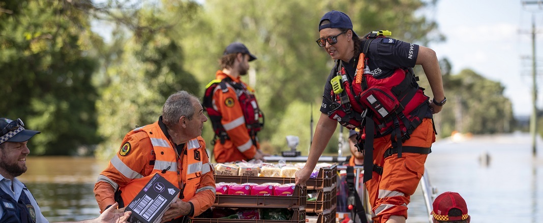 Surf rescue, police and SES workers in a boat over flood water with essential supplies