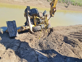 A backhoe that has rolled down the embankment of a flooded creek