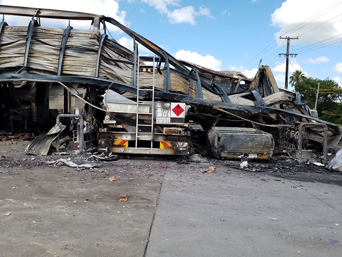 A service station that has extensive fire damage, including a collapsed and charred canopy which has fallen onto a burned truck.