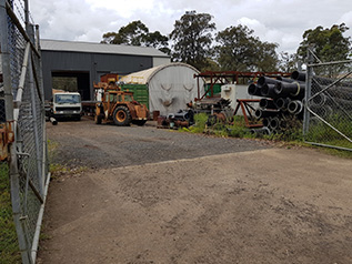 An open gate leading to a driveway with a shed and vehicles