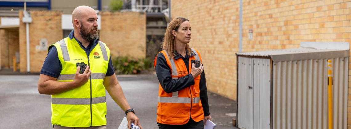 Female inspector wearing orange vest and male inspector wearing yellow vest wearing body worn video